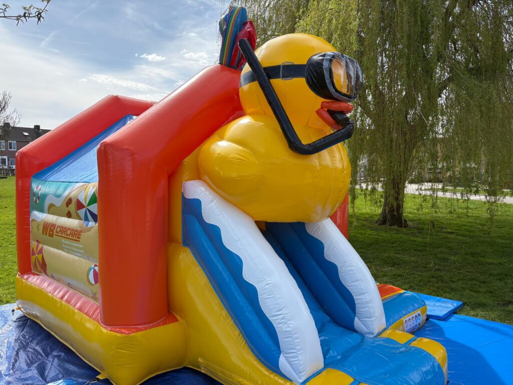 Het badeend springkussen met glijbaan van WB Springkussenverhuur opgesteld op een grasveld